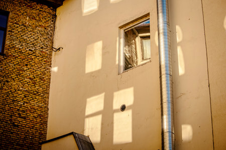 Window in yellow wall with reflections of other windows on the wall as well as a water pipe and a...
