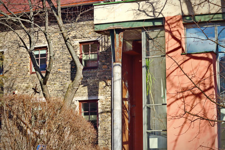 Old brown brick wall building behind leafless trees and a corner of a new red building with glass corner window with palm treeの写真素材