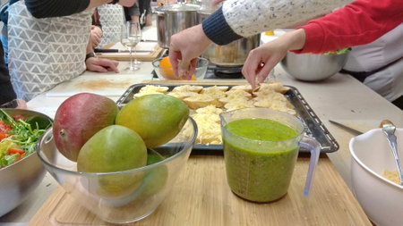 People preparing food sprinkling cheese on something on baking pans, table view on smoothie and mangoes with hands over the foodの写真素材