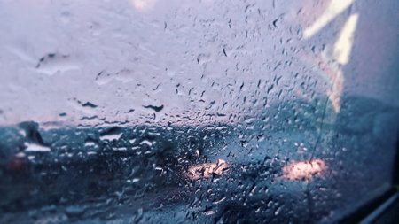Rain and dew drop on the car glass window during raining condensation with visible car driving near...
