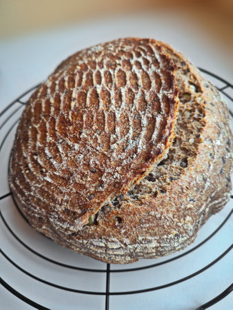 freshly baked artisanal whole wheat sourdough bread with rustic crust cooling on a round metal rack surfaceの写真素材