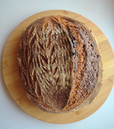 freshly baked artisanal whole wheat sourdough bread with rustic crust cooling on a round metal rack surface side viewの写真素材