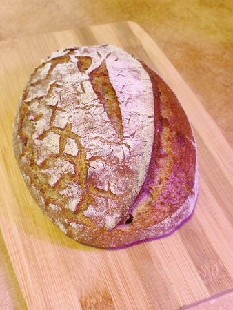 freshly baked artisanal whole wheat sourdough bread with rustic crust cooling on a wooden board surface front viewの写真素材