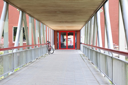 Contemporary covered pedestrian corridor leading to bright red entrance doors with bike parked alongside. Excellent for modern architecture, institutional buildings, public spaces, urban design, and accessible entrance concepts.の写真素材