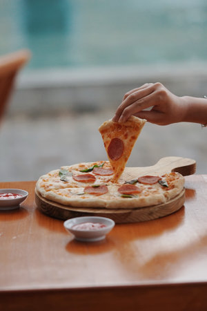 woman's hand is picking up a slice of pizza on a blurry backgroundの写真素材