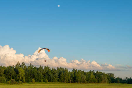Powered paraglider flying against blue sky with clouds and moonの写真素材