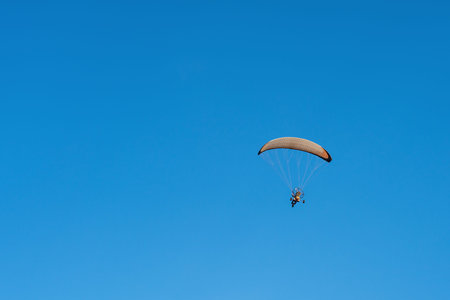 A powered paraglider trike flying over clear blue sky back view