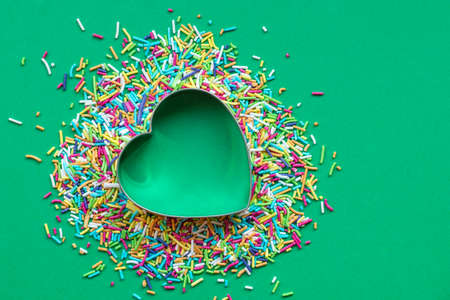 Colored sprinkles with a heart-shaped cookie cutter on green paper background. Christmas and love concept.の写真素材