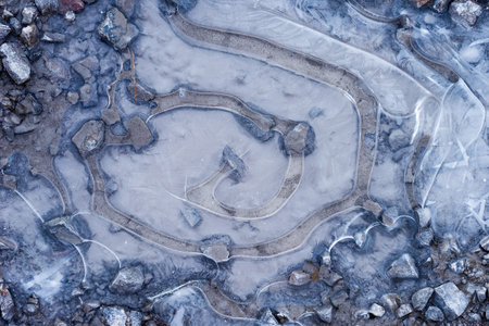 Frozen puddle on a rocky road top view. Snail look pattern made of ice during wintertime. Frozen...