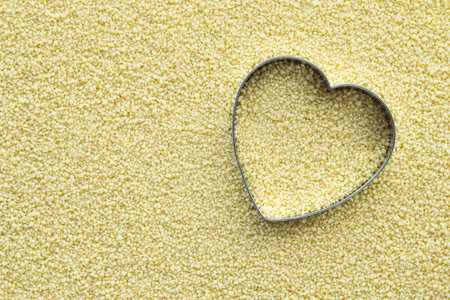 Heart cookie cutter placed on couscous groats background. The idea for Valentine's Day card with copy space. Food background.の写真素材