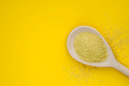 Couscous groats (made of durum hard wheat) in wooden spoon isolated on yellow background with copy space. Healthy food concept in flat lay view.の写真素材