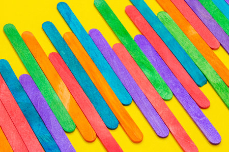 Colored popsicle sticks arranged side by side. Wooden ice cream sticks on yellow paper. Multicolored...