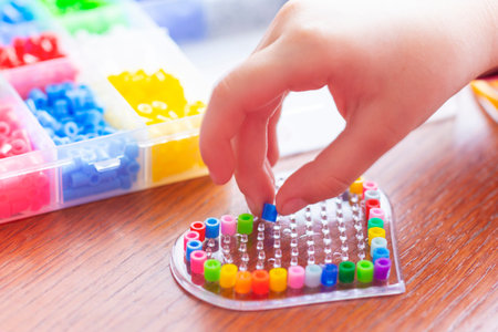 A child making a heart from plastic beads piece by piece. Educational activity for kids. Motor...