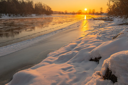 Golden rays of the sun break through the chilly morning air, reflecting on the icy surface of the...