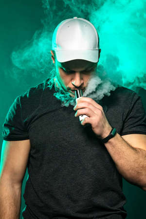 vaping man holding a mod. A cloud of vapor. dark blue background.の写真素材