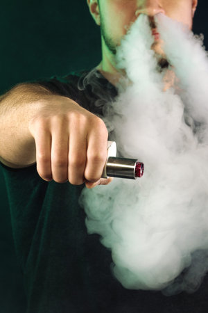vaping man holding a mod. A cloud of vapor. dark background.