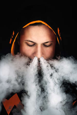 vaping man holding a mod. A cloud of vapor. dark blue background.の写真素材