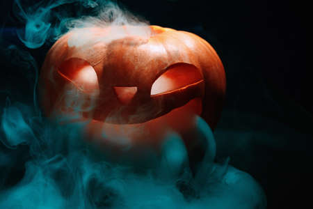 Halloween pumpkin lantern with dry leaves with burning eyes on black backgroundの写真素材