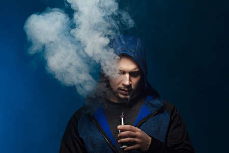 vaping man holding a mod. A cloud of vapor. dark blue background.の写真素材