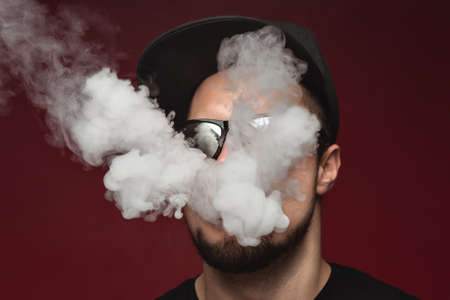 Vaping man. A cloud of vapor. red background.の写真素材