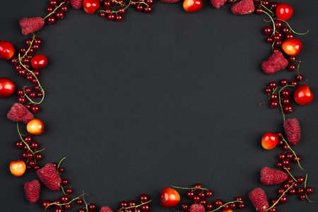 Frame of ripe red currant berries cherries and raspberries on a black backgroundの写真素材
