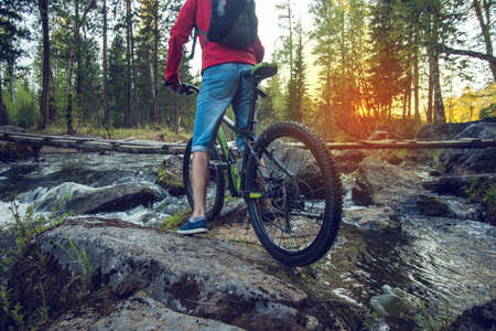 Ride on bike on the stones on the river at sunset. Sport and active life concept in the summer timeの写真素材