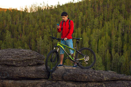 Cyclist on a cliff with the mountain bike talking on the phone to the forest in the backgroundの写真素材