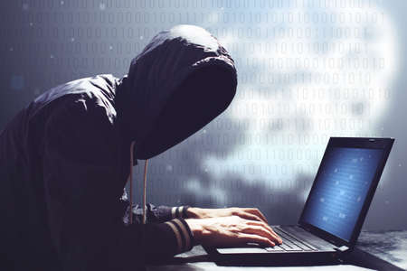 An adult online anonymous internet hacker with invisible face sitting at the laptopの写真素材
