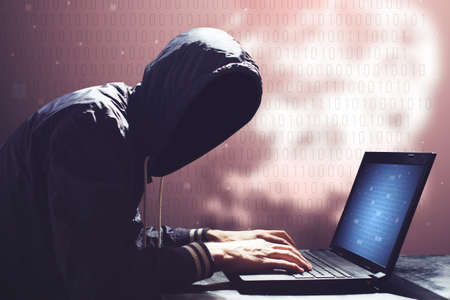 An adult online anonymous internet hacker with invisible face sitting at the laptopの写真素材
