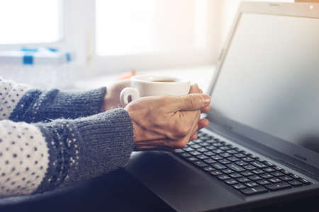 cropped view of the hands of a man is working at a laptop drinking coffeeの写真素材