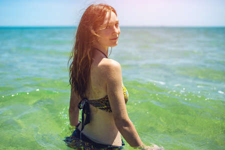 happy wet young woman standing back in blue sea water, concept of vacation in warmer climes, the trip to the seaの写真素材
