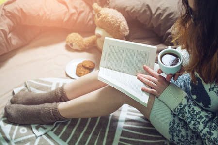 girl reading book in bed in a sweater and warm socks keeping your coffee in hand in the morning. the concept of new year mood.の写真素材