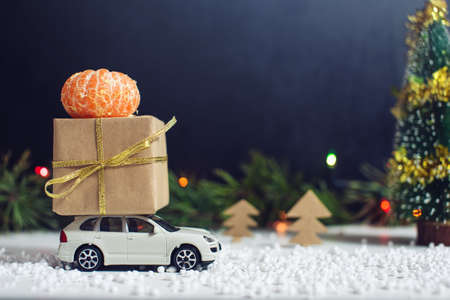 Toy car carries a gift for Christmas and New Year in the snow, on a black background.の写真素材