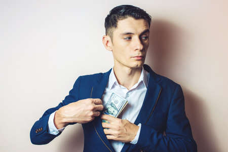 man businessman in suit taking notes, bills of dollars in his pocket as a bribe. the concept of corruption and briberyの写真素材