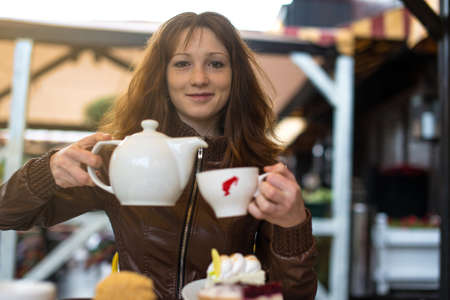 Portrait of young happy smiling woman with teapot and cup, in cafeの写真素材