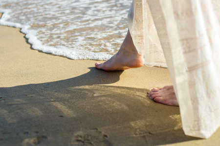 girl walks barefoot in the sand on the beach in a white dressの写真素材
