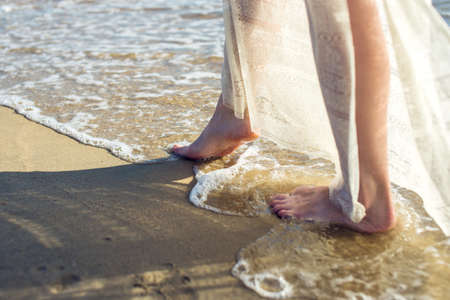 girl walks barefoot in the sand on the beach in a white dressの写真素材