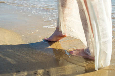 girl walks barefoot in the sand on the beach in a white dressの写真素材