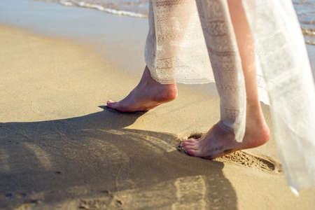 girl walks barefoot in the sand on the beach in a white dressの写真素材
