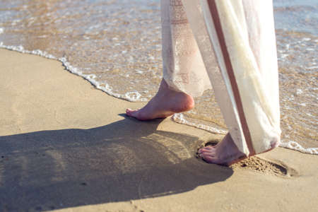 girl walks barefoot in the sand on the beach in a white dressの写真素材