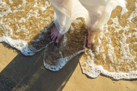 girl walks barefoot in the sand on the beach in a white dressの写真素材