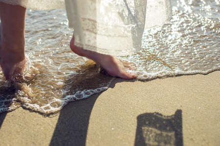 girl walks barefoot in the sand on the beach in a white dressの写真素材