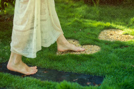 girl walking barefoot on the stones in heart shape on green grass, concept of love for the natureの写真素材
