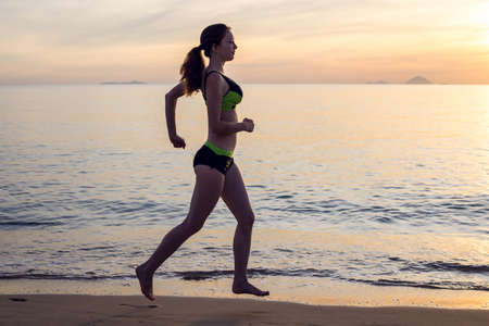 Woman running on beach at sunset, sea backgroundの写真素材