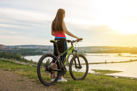 A woman cyclist on a mountain bike looking at the landscape of river. Adventure travel on bike....