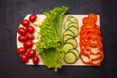 Vegetables, onion, garlic, tomato, cucumber, paper, salad, chopping board and knife on a table on black backgroundの写真素材