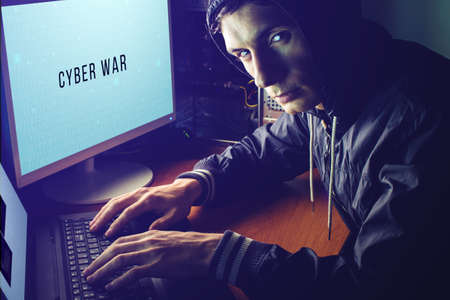 young hacker in the dark breaks the access to steal information and infect computers and systems. concept of hacking and cyber terrorismの写真素材