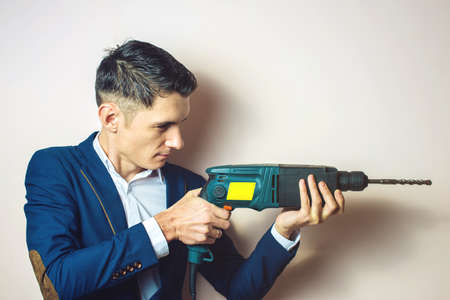 young man in suit holds in hand a power drill and works with it, a businessman for dirty workの写真素材