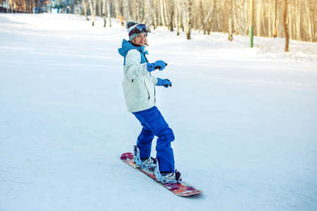 female snowboarder snowboarding down the mountain among the trees at sunset, concept of sport and active lifestyleの写真素材