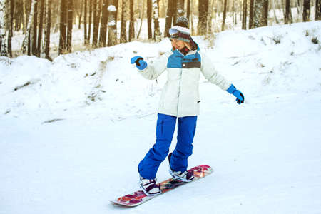 female snowboarder snowboarding down the mountain among the trees at sunset, concept of sport and active lifestyleの写真素材